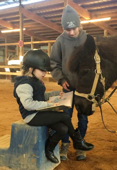 child reading to a black pony